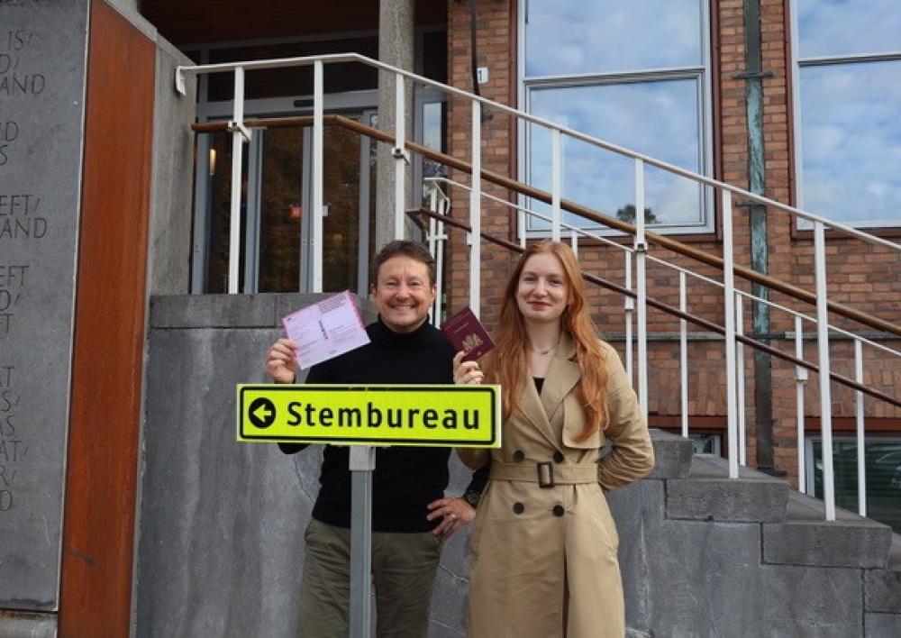 Twee Aalsmeerders met paspoort en stempas voor het raadhuis bij het bord Stembureau