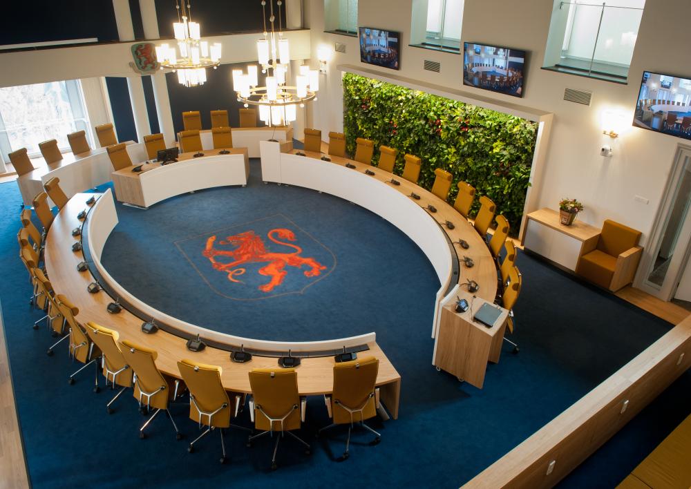 Raadzaal van Aalsmeer met lege stoelen. Het tapijt is blauw met een rode leeuw erop.