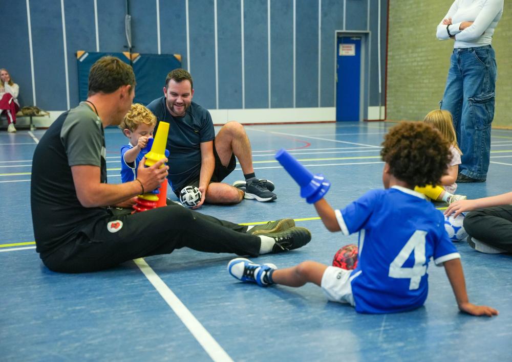 Kinderen en coaches sporten en spelen in sportzaal met voetbalspullen