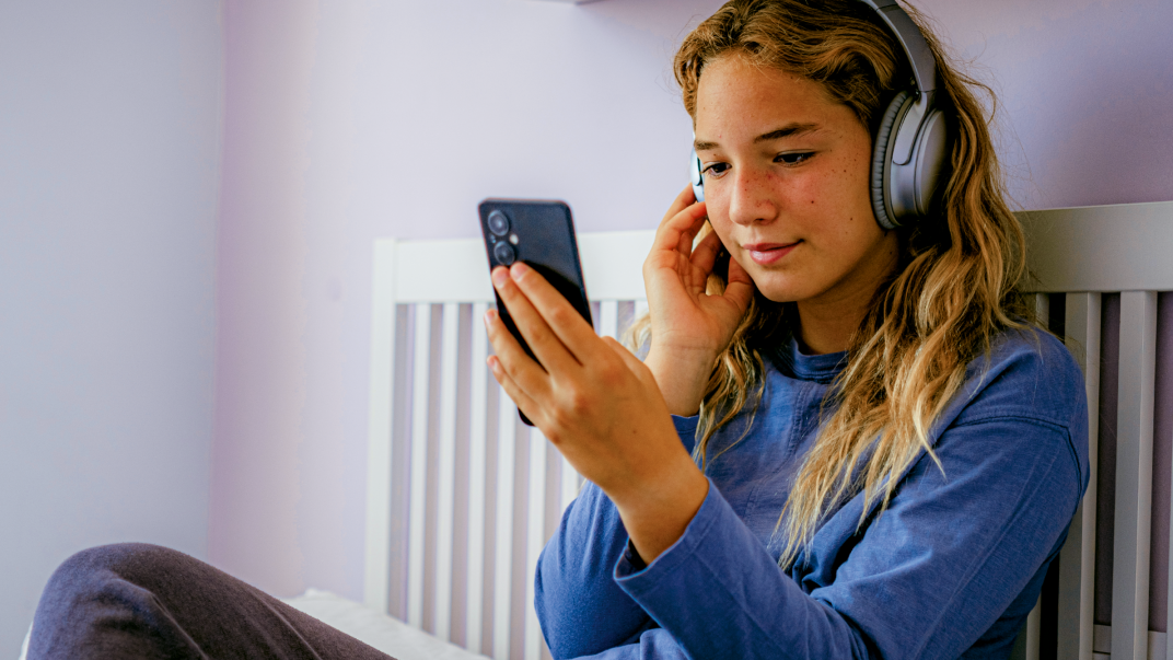 Tienermeisje met koptelefoon op het hoofd en mobiel in de hand